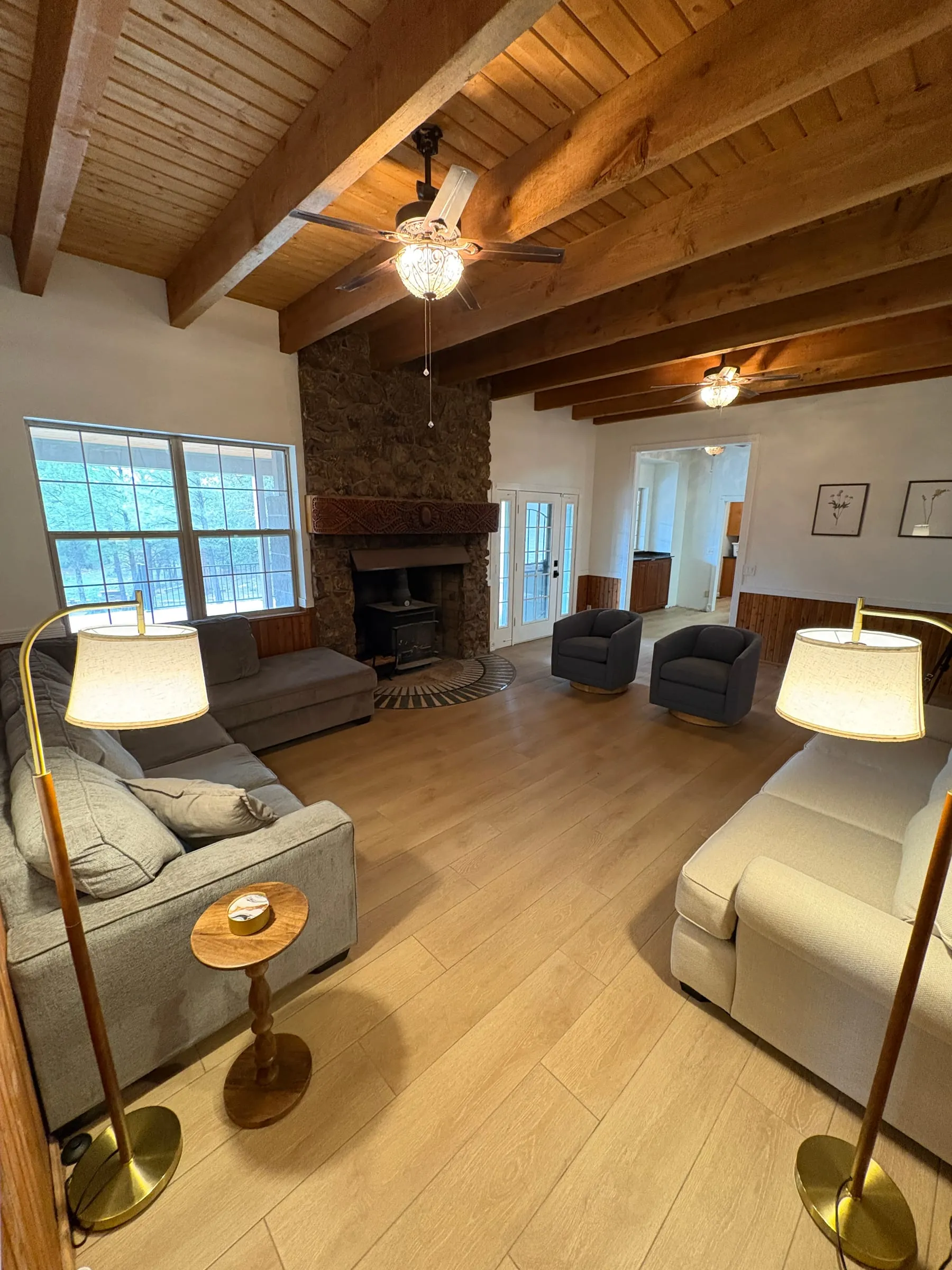 The family room — sofas and armchairs around a floor-to-ceiling stone fireplace, under a vaulted ceiling with exposed beams and tall windows on two sides.