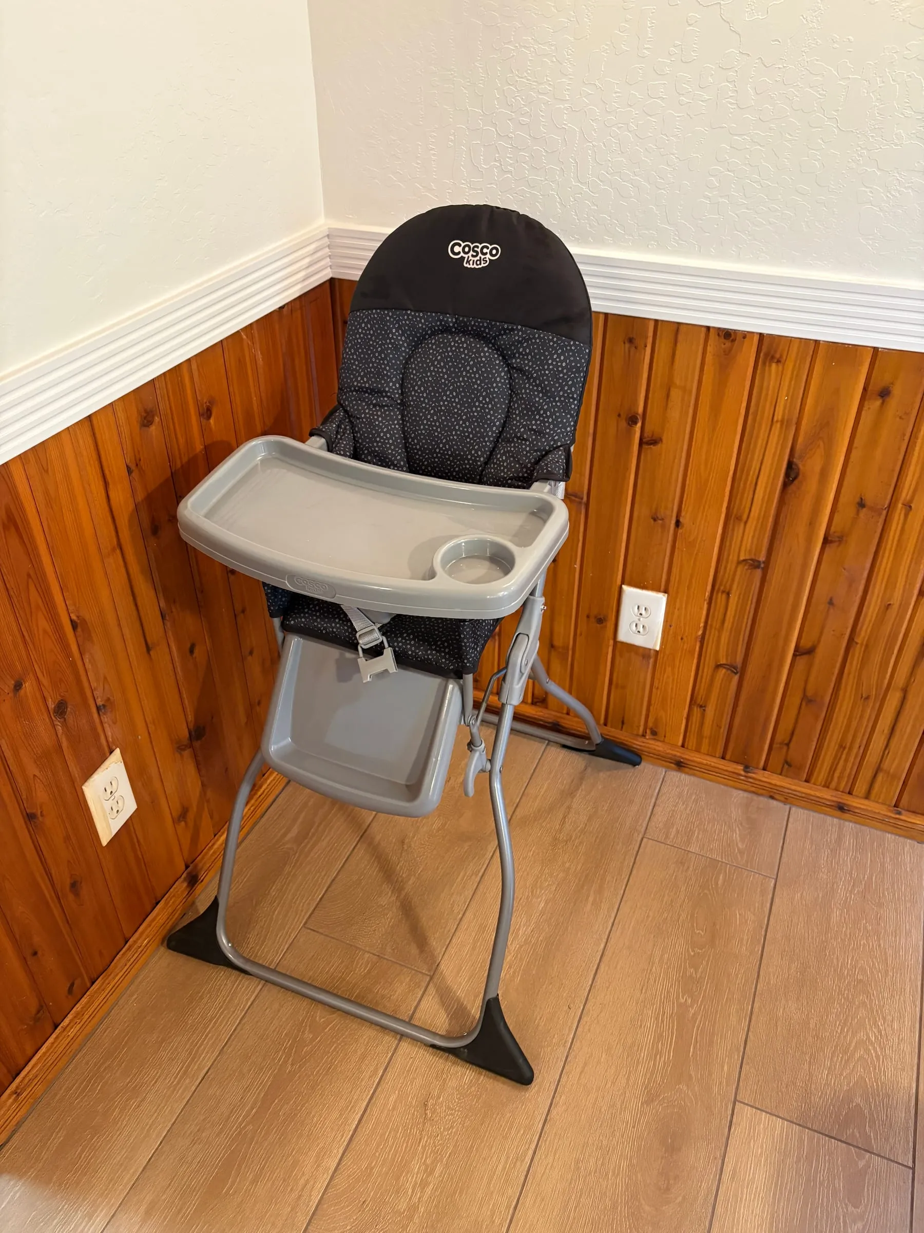 A folding high chair with a removable tray, set against the wood-panelled wall in the dining area.