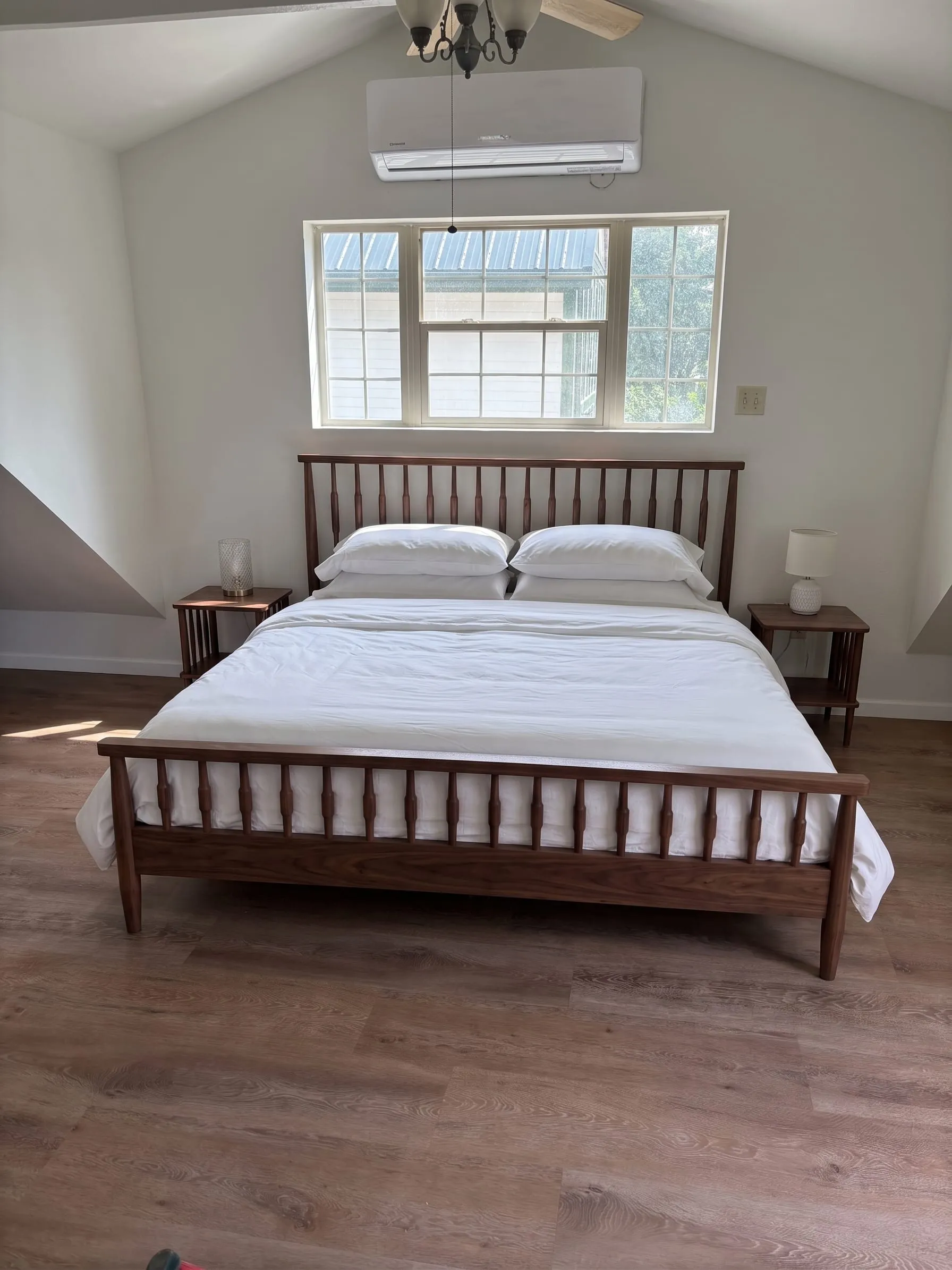 Nora’s studio — a king bed with a slatted walnut frame under a vaulted ceiling, with a wall-mounted mini-split unit above the window.