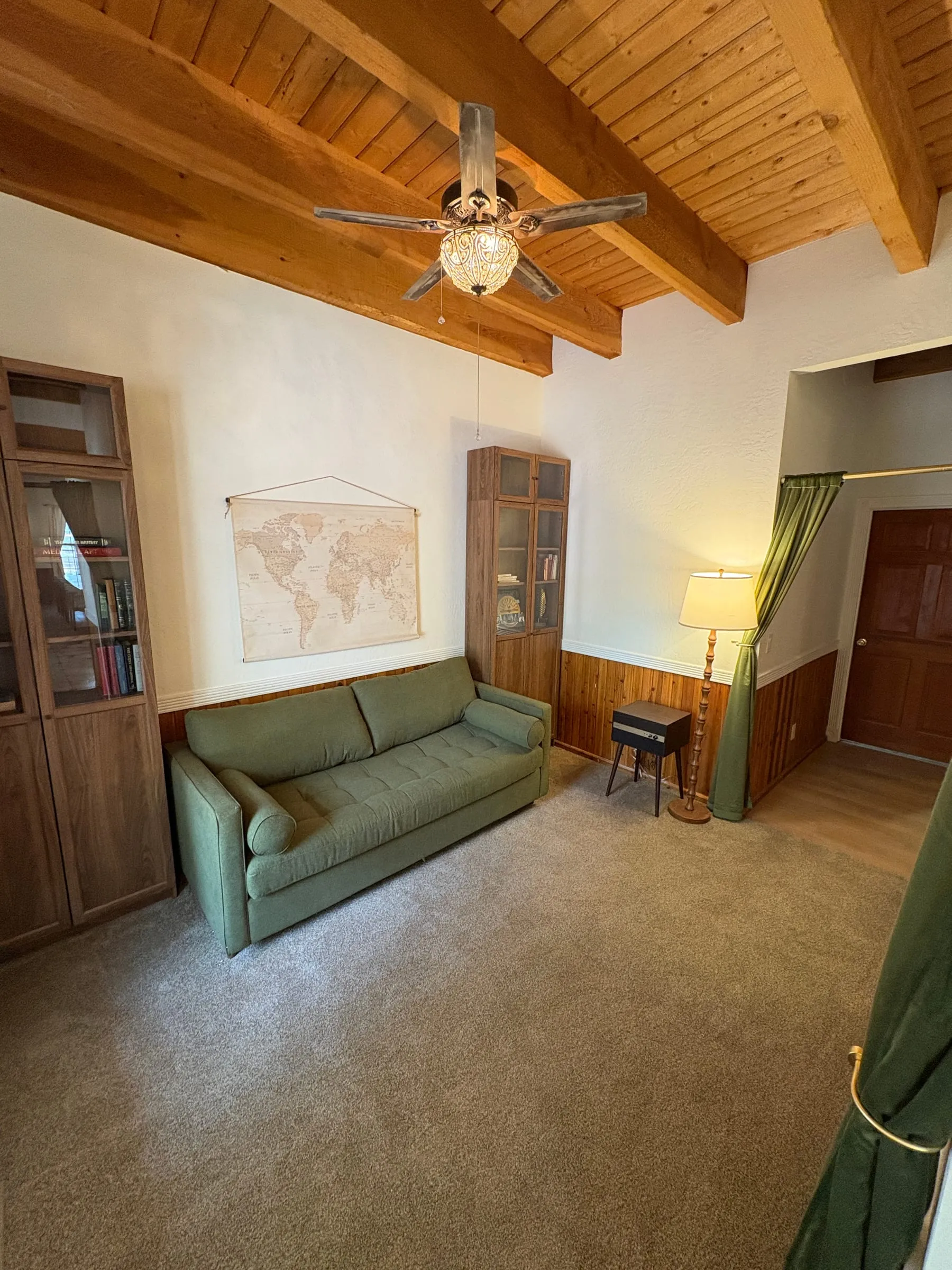 The Study — a green convertible sofa between two glass-fronted bookcases, under an exposed wood-beam ceiling, with a framed world map on the wall.