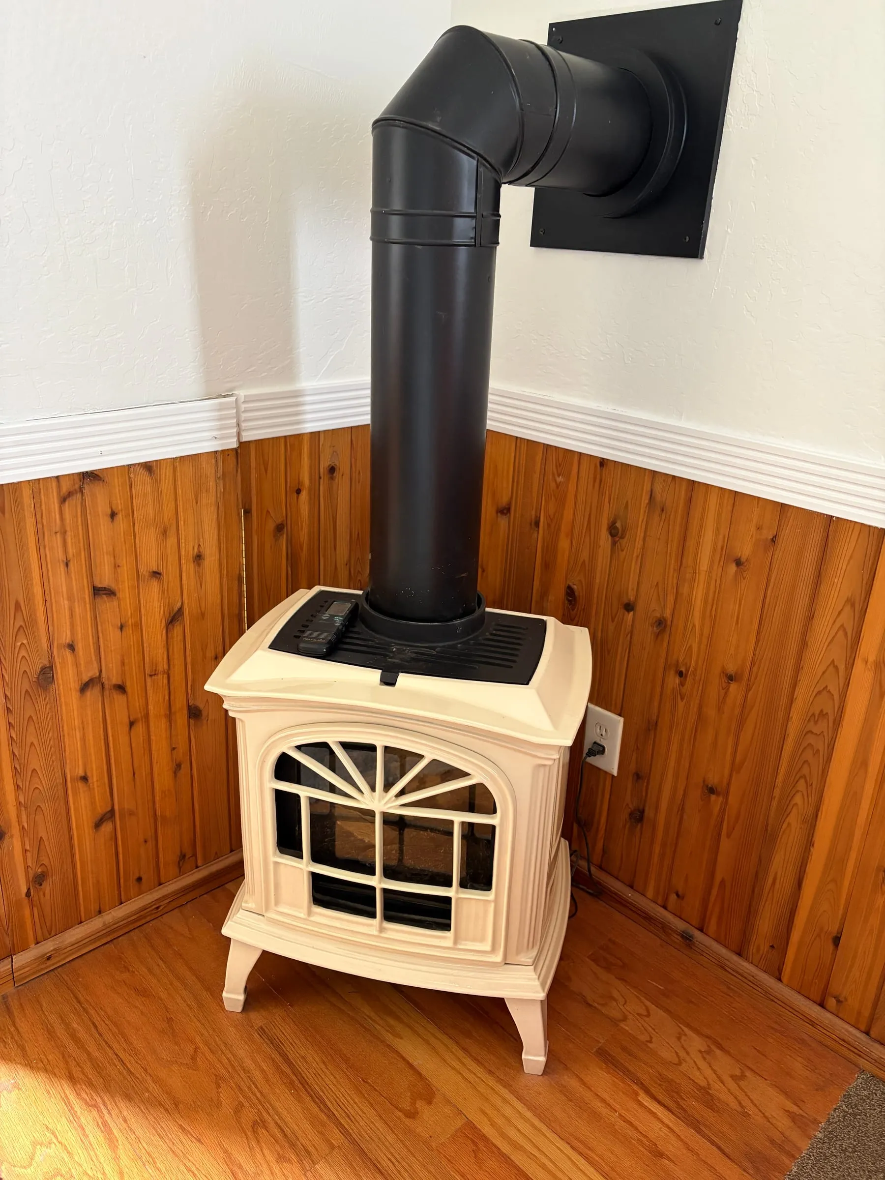 A cream-coloured gas stove with a black flue, against a wood-panelled wall. Harper’s Room and Jane’s Room each have one for heat, controlled from inside the bedroom.