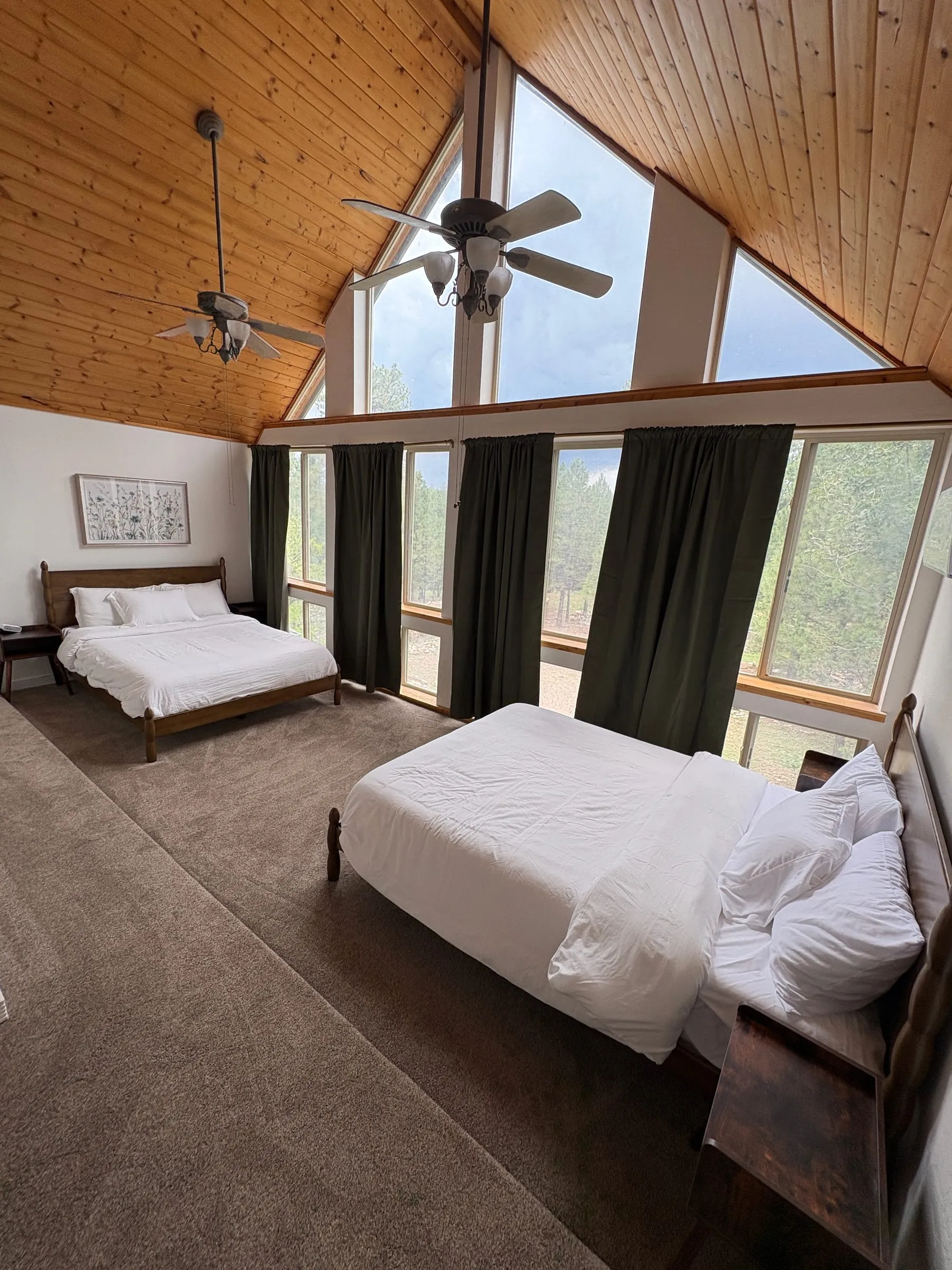 The Window Room — a queen bed beneath a high wood-panelled ceiling, with tall windows along one wall looking into the forest.